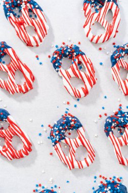 Dipping pretzels twists into melted chocolate to make red, white, and blue chocolate-covered pretzel twists.