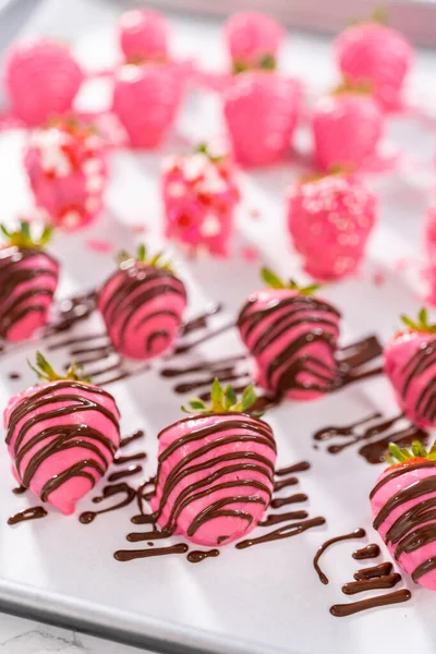 Decorating chocolate-covered strawberries with chocolate drizzles and sprinkles.