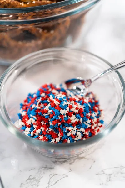 Dipping pretzels twists into melted chocolate to make red, white, and blue chocolate-covered pretzel twists.