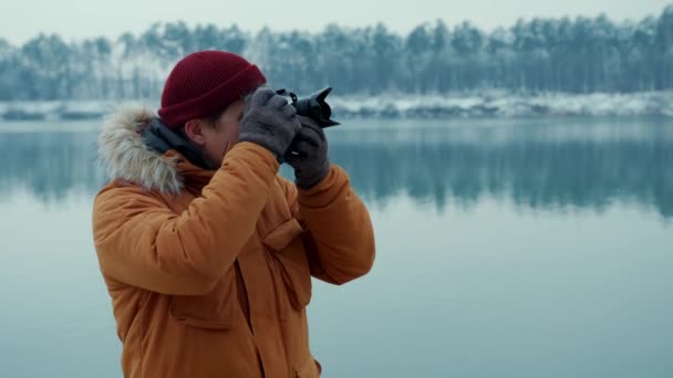 Portrait man photographer takes pictures of a lake in the winter forest. on a professional camera — Stockvideo
