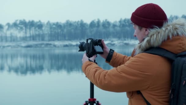 수컷 사진 작가가 눈내리는 날씨에 아름다운 카르파티아 산맥의 숲 가장자리를 촬영하기 위해 삼각대에 카메라를 부착 한다 — 비디오