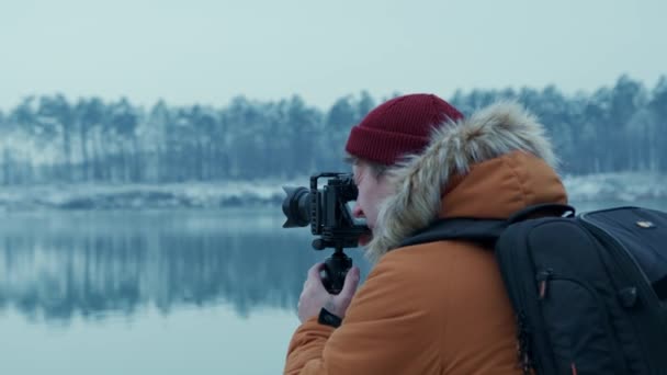 Adventure photographer takes pictures of a lake in the winter forest. on a professional camera — Stok Video