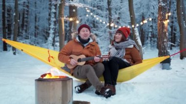 Couple guy with a girl sitting by the fire with a singing fun with a guitar winter