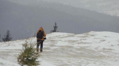 Şiddetli bir kar fırtınası sırasında turist fotoğrafçısı bir dağın tepesinde yürür.