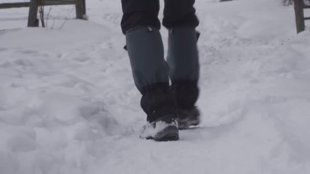 Man feet in winter warm, comfortable shoes take a step on a snowy road in the park on a winter walk. — Stock Video