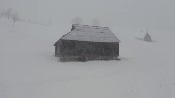 Fantástico filme de inverno com um homem de casaco amarelo e uma cabana de madeira nas montanhas nevadas durante uma tempestade de neve. Aviação — Vídeo de Stock