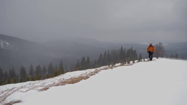 L'uomo cammina lungo il sentiero sulla cima di una collina innevata. L'uomo con una giacca gialla cammina l'inverno camminando. — Video Stock
