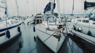 Mavi yelkenli gün batımında yat limanındaki bir rıhtıma demirlemiş. Renkli bulutlar, suda yansımalar. Yelkencilik, eğlence teması. Güney Norveç Köyü