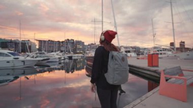 Kulaklıklı, tanınmayan genç bir kadın denizin üstünde gün batımının tadını çıkarıyor.