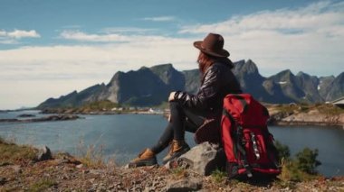 Sırt çantalı bir kız denize bakan bir kayanın üzerinde oturur ve muhteşem manzaranın tadını çıkarır.