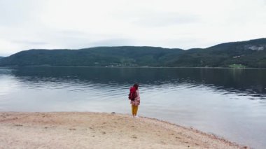 Büyük sırt çantalı mutlu bir turist kadın göle bakıyor ve doğaya bakıyor. Arka plan.