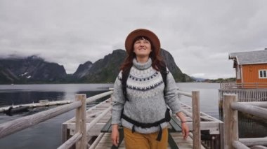 Gezgin ahşap iskeleye gider. Süveter, örgü şapka ve kırmızı bir sırt çantası giymişti. Arkadan bak. Lofoten Adaları Norveç.
