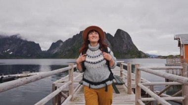 Gezgin ahşap iskeleye gider. Süveter, örgü şapka ve kırmızı bir sırt çantası giymişti. Arkadan bak. Lofoten Adaları Norveç.
