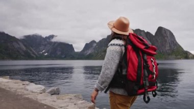 Gezgin ahşap iskeleye doğru yürür. örgü kazak ve kırmızı bir sırt çantası giymişti. Arkadan bak. Lofoten Adaları Norveç.