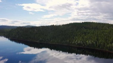 Hava aracının çektiği manzara çok güzel. Orman ormanı ve sakin göl. Su yüzeyinde yansıyan şişman beyaz bulutlar..