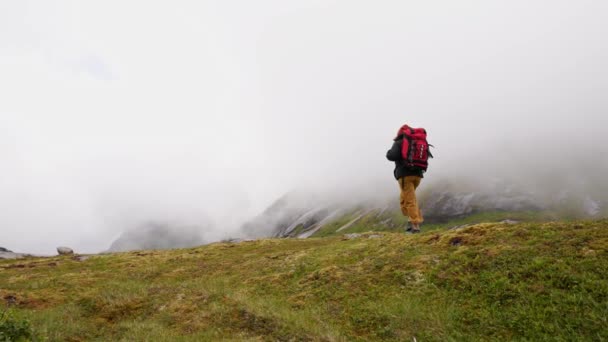 赤いバックパックを持つジャケットの女性観光客は ノルウェーの山の中で岩の上に霧の中を歩く 雨の日 — ストック動画