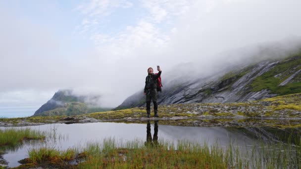 男性旅行ブロガー山の中でバックパックとスマートフォンのハイキングで写真を撮るインフルエンサーライフスタイルアドベンチャー夏のツアーノルウェーの屋外 — ストック動画