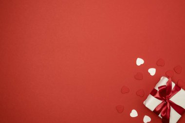 Gift box with red ribbon bow and hearts on red background. Valentine's Day background. Top view, text space