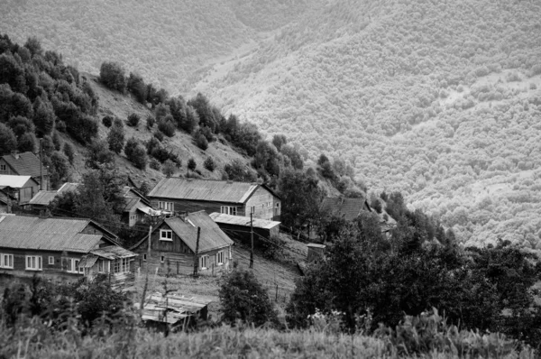 手前の山の緑の斜面にある小さな村と背景の緑の木で覆われた峡谷の反対側の斜面。 — ストック写真