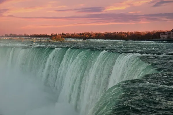 Зелені води річки Ніагара зливаються з краю водоспаду Хорсешо перед захопливим заходом сонця. Водоспад Хорс, також відомий як канадський водоспад, є найбільшим з трьох водоспадів. — стокове фото