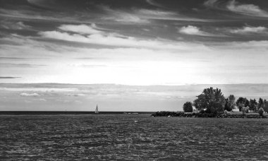 Beautiful seascape with cloudy sky, island with trees, and a small sailboat cutting waves in the wind