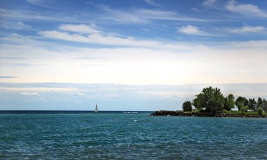 Beautiful seascape with cloudy sky, green island and a small sailboat cutting waves of turquoise waters