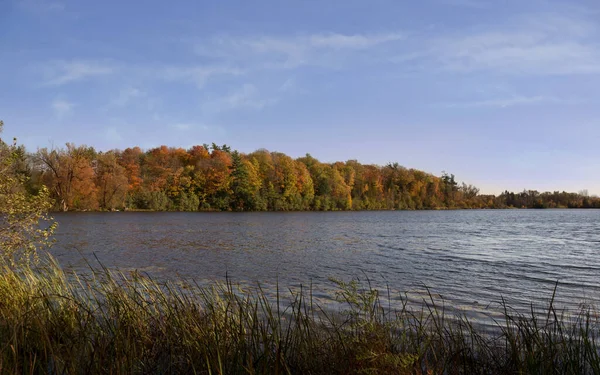 Beautiful autumn landscape view with Seneca lake surface reflecting blue sky and yellow orange red trees across the lake. King city, Ontario, Canada