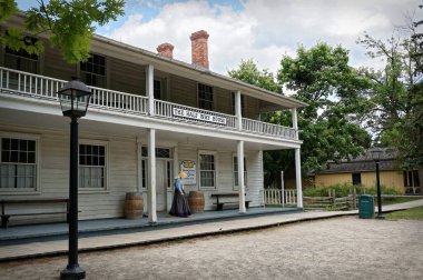 TORONTO, CANADA - 06: 21 2016: 19. yüzyıl kostümlü bir müze çalışanı, 1849 tarihli Black Creek Pioneer Village 'daki Half Way House Inn' den yürüyerek çıktı.