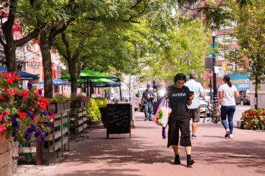 Toronto, Canada - 08 03 2018: Mild summer day scene on Front Street in St. Lawrence neighnorhood of Old Toronto with people walking beside restaurants street patios decorated with colorful flowerbeds.
