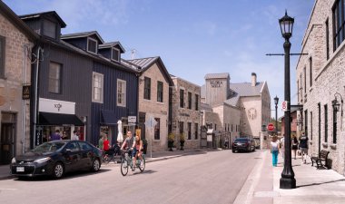 Elora, Ontario, Kanada - 05: 15 2022: Mill Street West boyunca yaz mevsimi manzarası, iki katlı eski evler ve Elora Mill binası, 1832 yılının arka planında Merkez Elora bölgesinde mavi gökyüzünün altında.