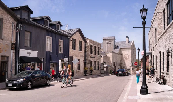 Elora, Ontario, Canada - 05 15 2022: Summertime view along Mill Street West with row of old two-storey houses and Elora Mill building of 1832 in background under blue sky in Elora community of Centre