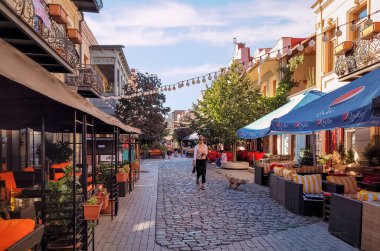 Tbilisi, Georgia - 07 23 2022: Young lady with a dog walking along Davit Aghmashenebeli Avenue in Downtown Tbilisi with street cafes lined up beside old two storey buildings of Old Tbilisi district.
