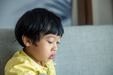Sarı tişörtlü, siyah saçlı Asyalı çocuk tabletin üzerinde oturuyor. Pencerenin yanındaki oturma odasındaki gri koltuğun tadını çıkarıyorum..