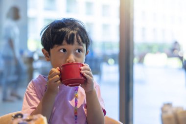 Pembe tişörtlü siyah saçlı Asyalı çocuk restoran tatilinde kahvaltı etmekten mutlu..