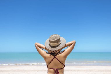 Tropikal sahilde bikinili ve hasır şapkalı genç kadınlar sıcak yaz günlerinde plaj okyanusunu seyretmenin keyfini çıkarıyorlar. Arka planda mavi deniz. Khao Lak, Phang Nga, Tayland. Yaz tatili kavramı.