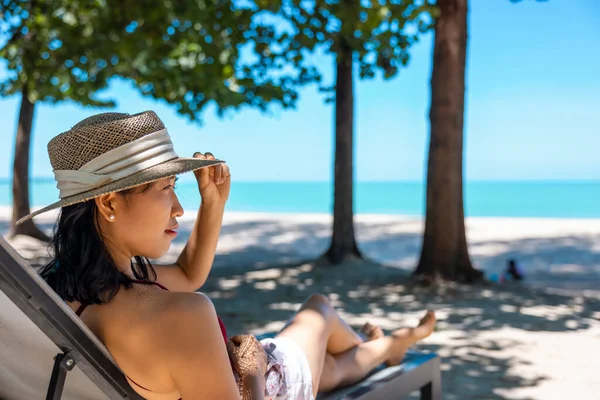 Kırmızı mayo ve hasır şapka giyen Asyalı manken deniz kenarında güneşlenir. Lüks otellerde dinlenen güzel bir kız. Spa, sağlık.