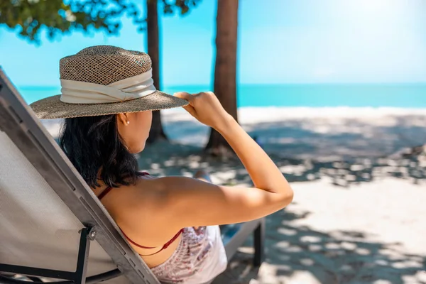 Kırmızı mayo ve hasır şapka giyen Asyalı manken deniz kenarında güneşlenir. Lüks otellerde dinlenen güzel bir kız. Spa, sağlık.