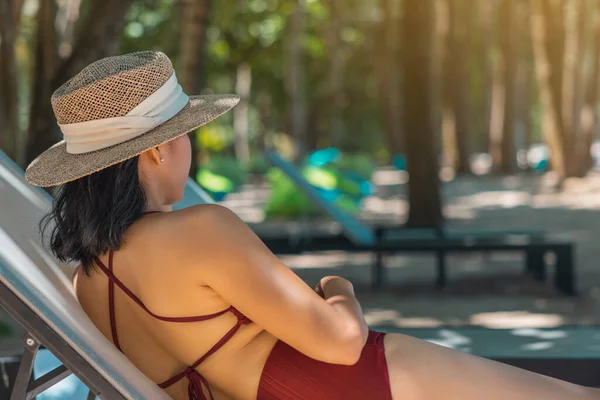 Kırmızı mayo ve hasır şapka giyen Asyalı manken kadın deniz kenarında güneşlenerek güneşleniyor. Lüks otellerde dinlenen güzel bir kız. Spa, sağlık.