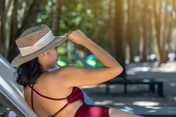 Kırmızı mayo ve hasır şapka giyen Asyalı manken kadın deniz kenarında güneşlenerek güneşleniyor. Lüks otellerde dinlenen güzel bir kız. Spa, sağlık.