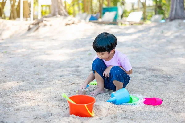 Asian boy sitting play sand with his sand toy set on enjoy tropical beach. Summer vacation concept.