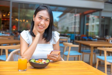 Kahvaltı yapan ve akıllı telefon oynayan bir kadın. Karpuz, papaya, kavun, tutku meyvesi, portakal suyu ve kahve gibi meyveler. gri bir paspasa yerleştirilmiş..
