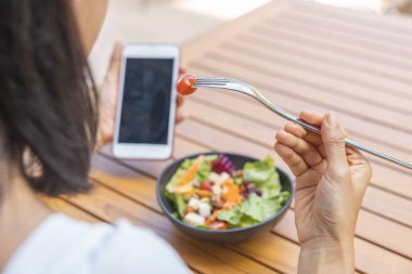 Kahvaltı yapan kadını kapat ve akıllı telefon oyununu oyna. Karpuz, papaya, kavun, tutku meyvesi, portakal suyu ve kahve gibi meyveler. gri bir paspasa yerleştirilmiş..