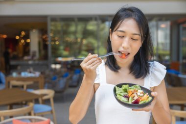 Kahvaltı yapan ve akıllı telefon oynayan bir kadın. Karpuz, papaya, kavun, tutku meyvesi, portakal suyu ve kahve gibi meyveler. gri bir paspasa yerleştirilmiş..