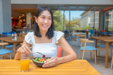 Kahvaltı yapan ve akıllı telefon oynayan bir kadın. Karpuz, papaya, kavun, tutku meyvesi, portakal suyu ve kahve gibi meyveler. gri bir paspasa yerleştirilmiş..