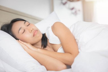 Young asian woman sleeping in bed at bedroom. she is lying on side and relax with eyes closed.