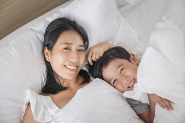 Young Asian woman and son sleeping in her bed and relaxing in bedroom. they are lying on the side and relax with their eyes closed. looking at the camera.