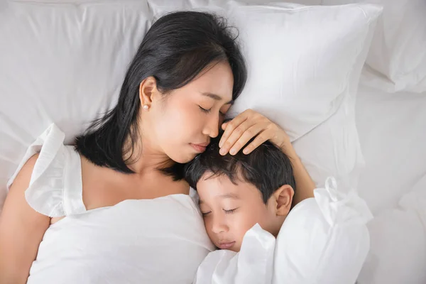 Young Asian woman and son sleeping in her bed and relaxing in bedroom. they are lying on the side and relax with their eyes closed.