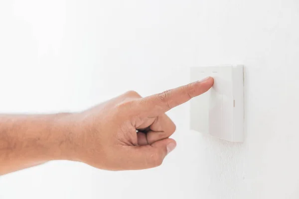 Close-up light switch of a male finger will turn on or off a light switch with white wall at home. white plastic mechanical switch mounted. Energy, energy, save electricity, copy space.