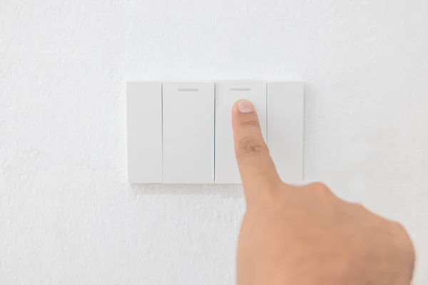 Close-up light switch of a male finger will turn on or off a light switch with white wall at home. white plastic mechanical switch mounted. Energy, energy, save electricity, copy space.