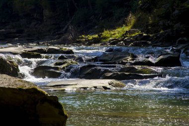 Güneşli bir yaz gününde nehrin şelalesi dağlardaki kayaların üzerinde akıyor. Manzara fotoğrafı iyi bir hava yaratıyor..